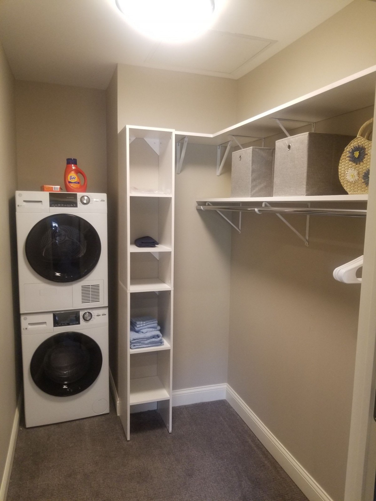 A tidy laundry room with a stacked washer and dryer, shelving units, and ample closet space.