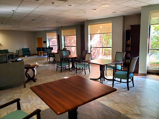 A cozy lounge area featuring chairs and tables, illuminated by natural light streaming through large windows.