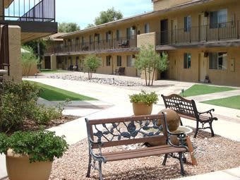 A tranquil courtyard featuring benches, potted plants, and a two-story building.