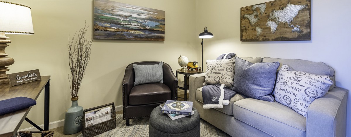 A cozy living room setup with an armchair, a sofa adorned with pillows, and decorative elements such as a lamp and wall art.