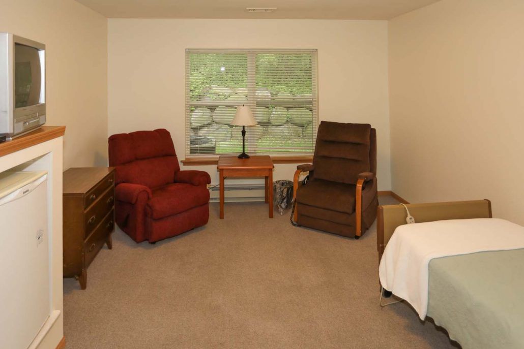 A cozy living room with two recliner chairs, a small table with a lamp, and a large window overlooking greenery.