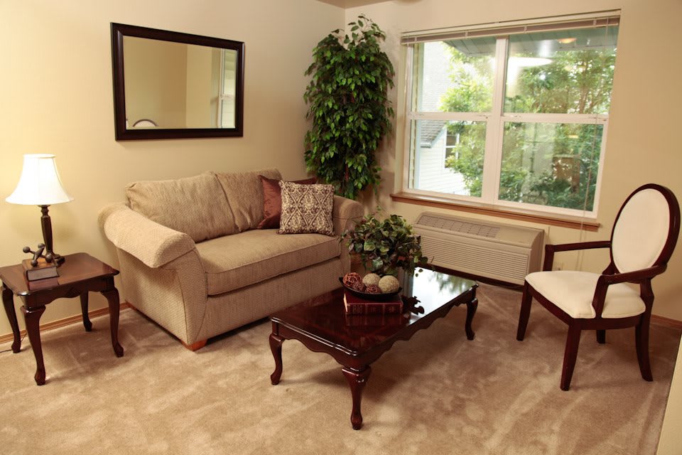 A cozy living room with a sofa, armchair, coffee table, and large window providing natural light.