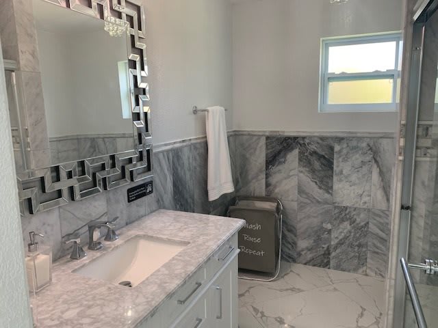 A modern bathroom with marble tiles, a sink, and a decorative mirror.