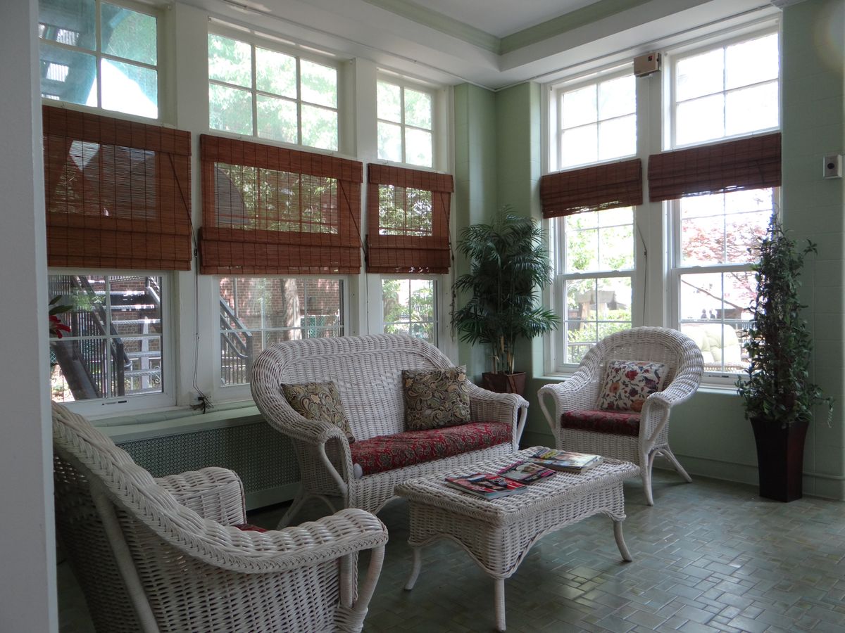 A cozy sunroom featuring wicker furniture, indoor plants, and abundant natural light.