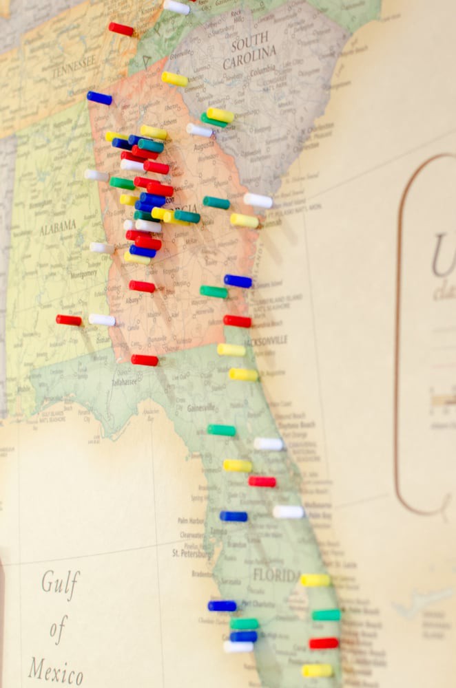 A wall map with various colored push pins marking specific locations.