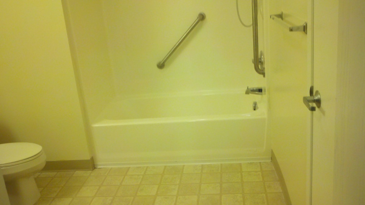 A bathroom with a bathtub featuring a grab bar and showerhead, tiled floor.