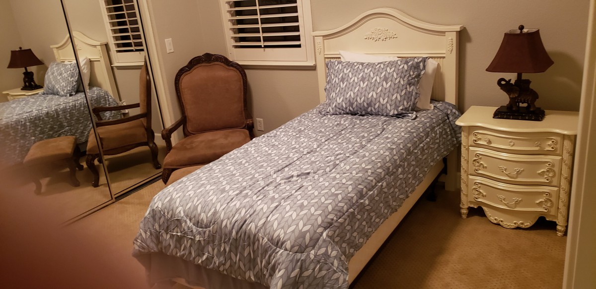 A cozy bedroom featuring a single bed with patterned bedding and a wooden chair.