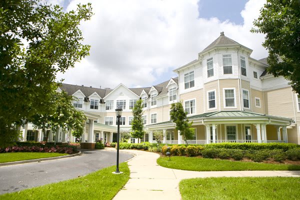 A large, elegant residential building surrounded by landscaped gardens and a winding pathway on a cloudy day.