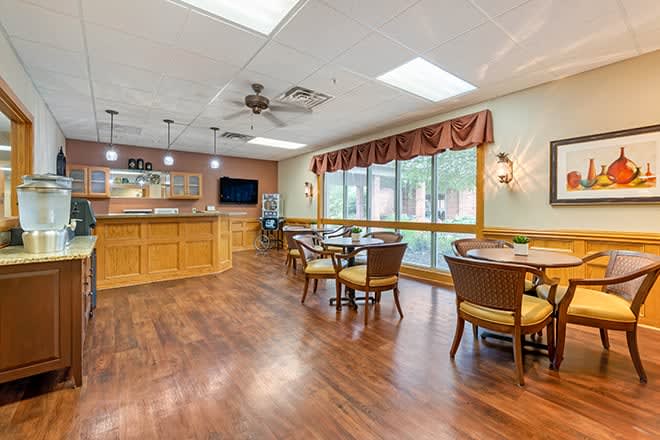 A cozy dining room with wooden flooring, round tables, and ample natural light.
