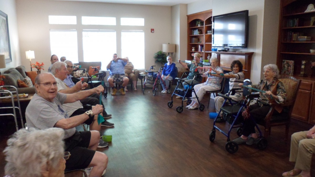 A group of seniors participating in a seated exercise session inside a community room.