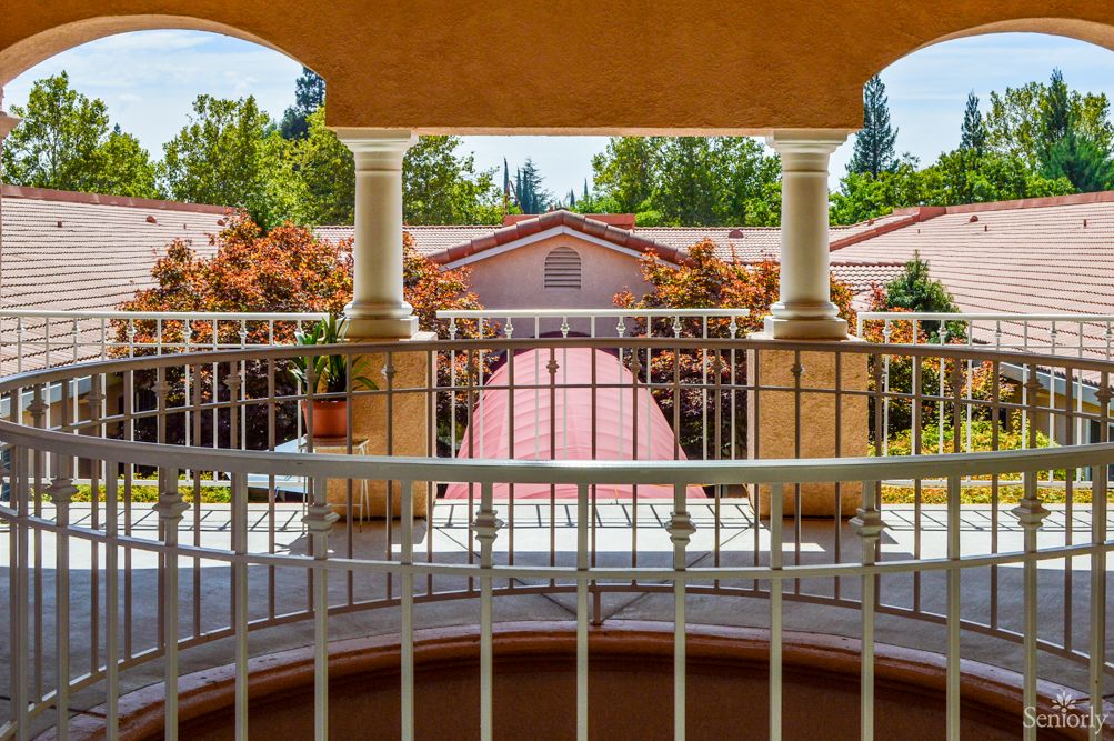 A sunny view from a balcony with columns and railings overlooking a courtyard.