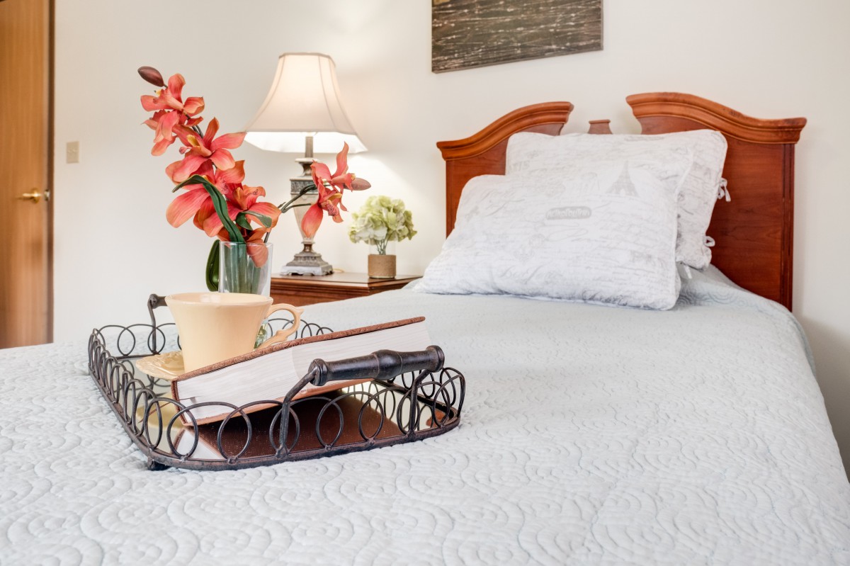 A cozy bedroom with a neatly made bed, featuring a decorative tray with flowers and books.