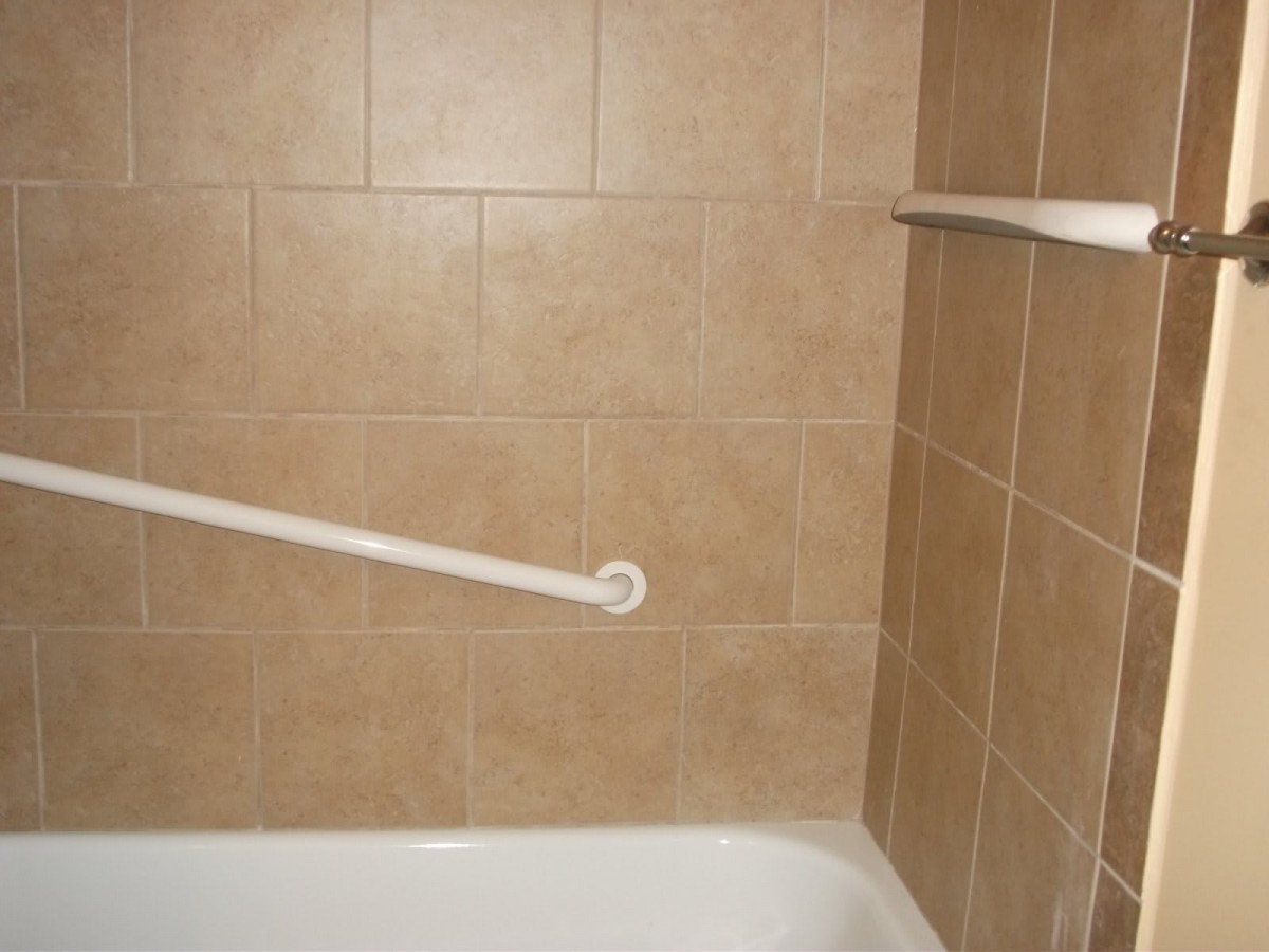A tiled bathroom corner featuring a bathtub and a safety grab bar.