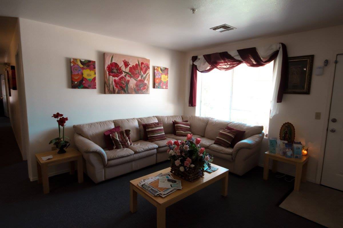 A cozy living room featuring a sectional sofa, coffee table with a floral centerpiece, and decorative artwork on the walls.