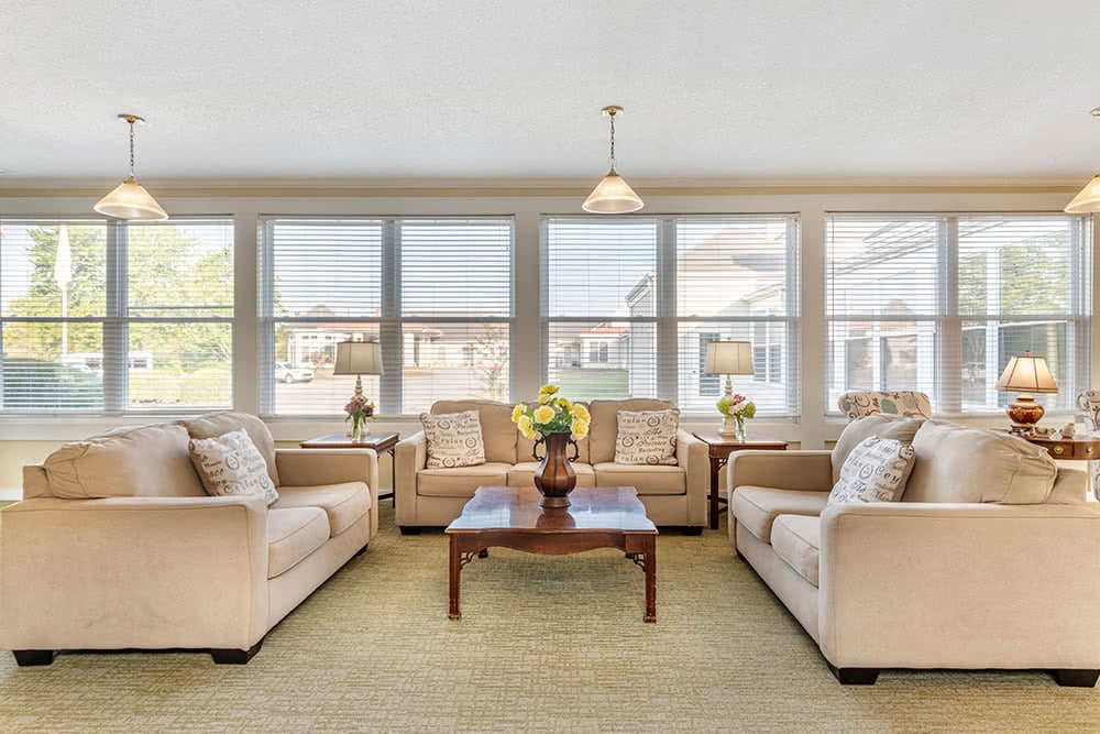 A bright and spacious living room with neutral-colored sofas and a wooden coffee table, surrounded by large windows.