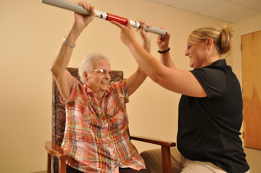 An elderly woman engages in an exercise session with the assistance of a caregiver, focusing on strength and mobility.