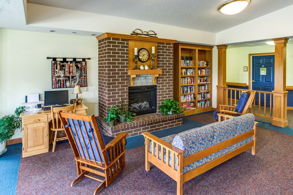 A cozy living room featuring a brick fireplace, wooden furniture, and a bookshelf.