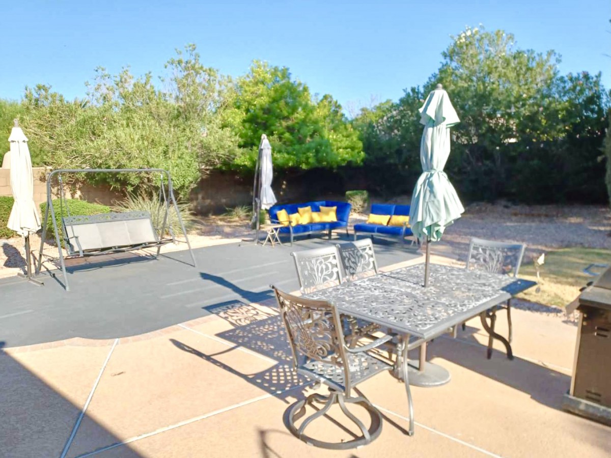 A sunny backyard patio with metal furniture and an umbrella.