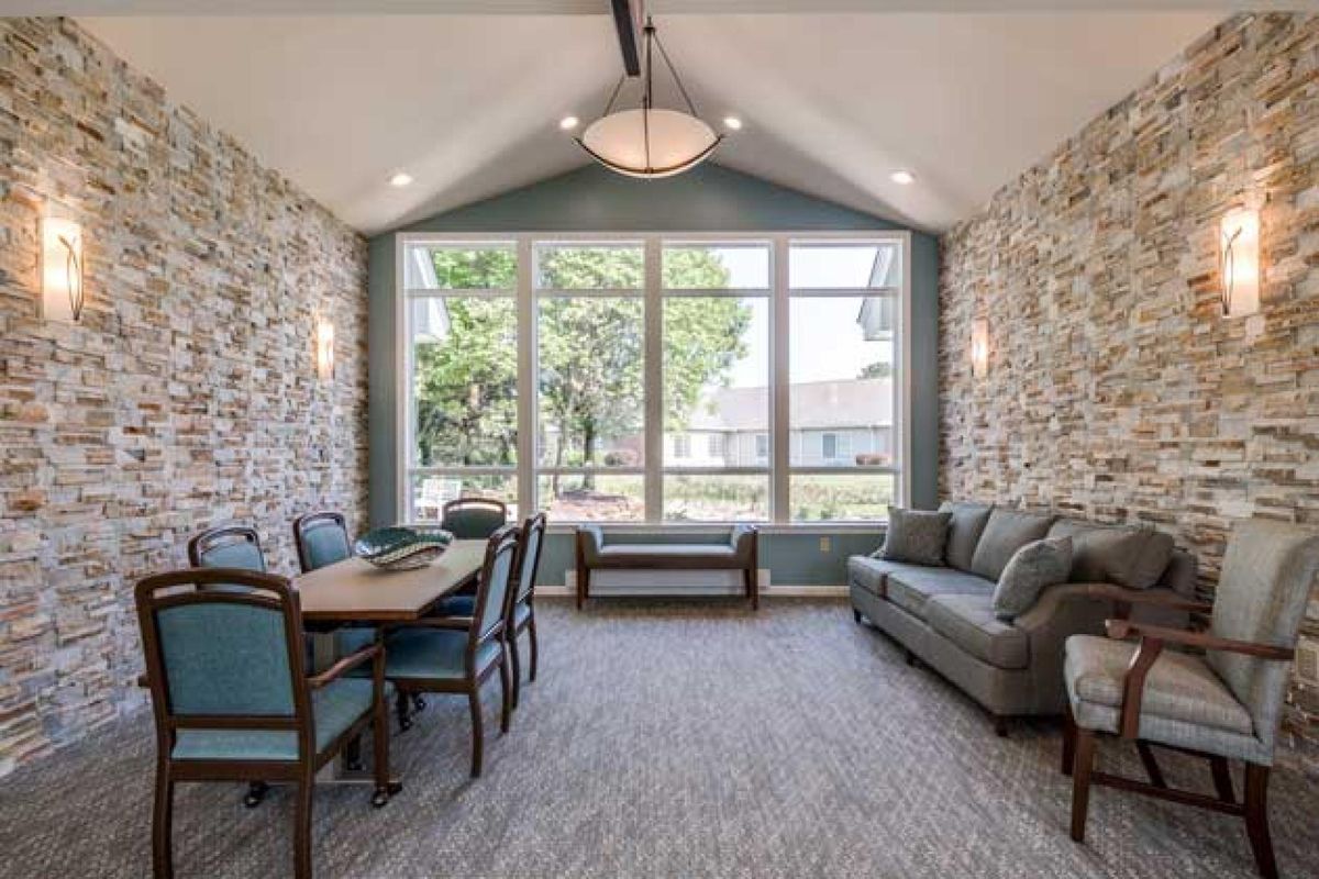 A cozy living space with a dining table and sofa, featuring stone walls and large windows allowing ample natural light.