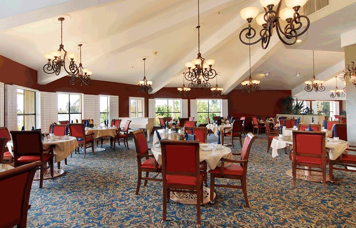 An elegant dining room with chandeliers, red chairs, and neatly arranged tables.