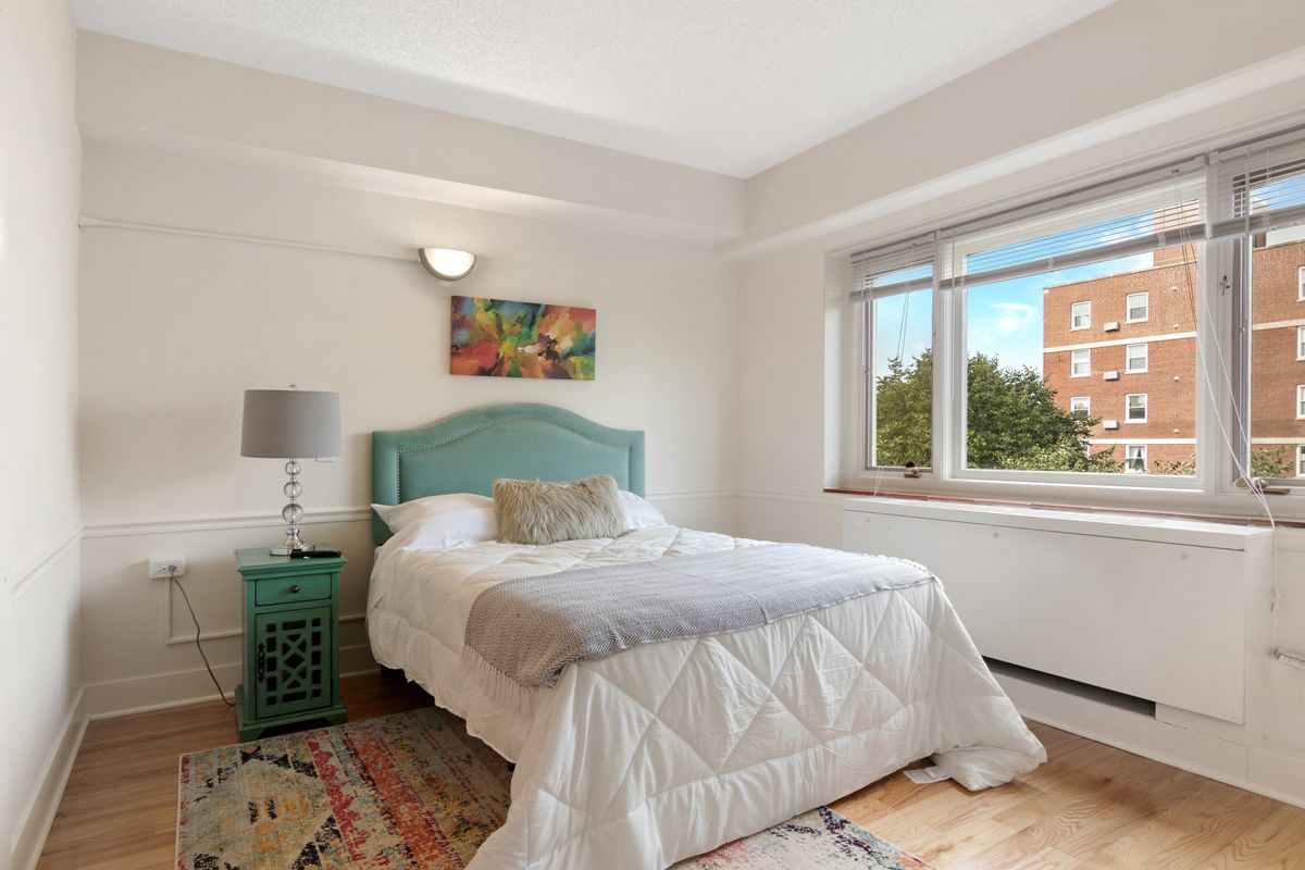 A cozy bedroom with a bed, artwork above the headboard, and a window providing natural light.