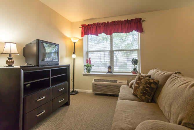 A cozy living room with a sofa, television, and a large window with red curtains.