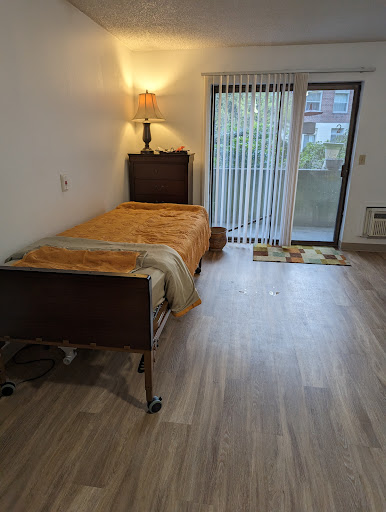 A cozy bedroom featuring a single bed with an orange blanket, complemented by a lamp and a sliding door that leads to the outside.