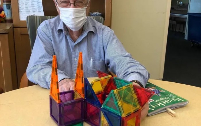 A man wearing a mask sitting at a table with colorful construction blocks.