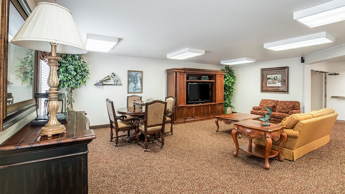A cozy living area featuring traditional furnishings, a dining table, entertainment center, and indoor plants.