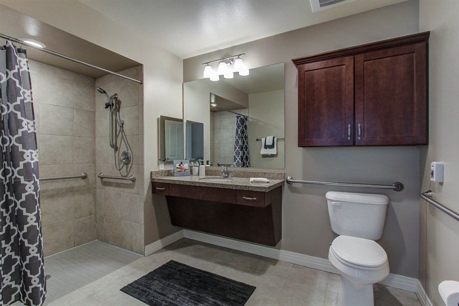 A modern bathroom featuring a vanity with a large mirror, shower area, and toilet.