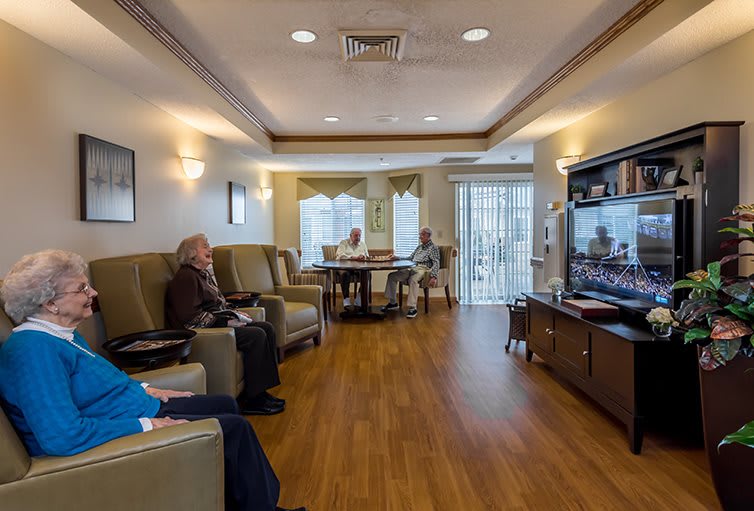 Elderly residents sit in a comfortable living room watching television in a retirement home.