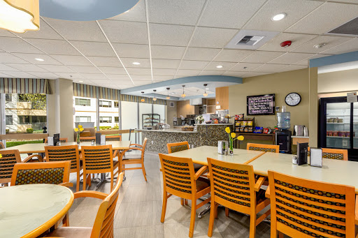 A bright and modern dining area featuring wooden tables and chairs, with a view of the kitchen.