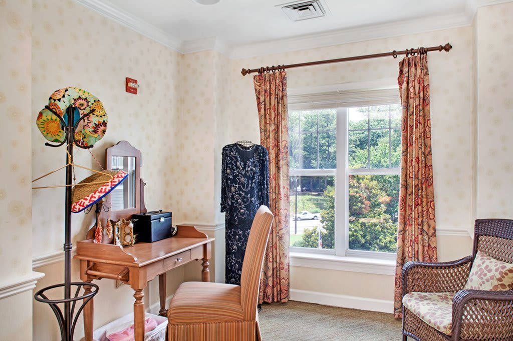 A cozy office space with a wooden desk and chair, featuring a large window with patterned curtains allowing natural light to fill the room.