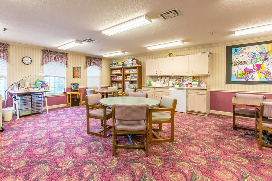 A cozy dining area with a round table, chairs, kitchenette, and vibrant carpet.