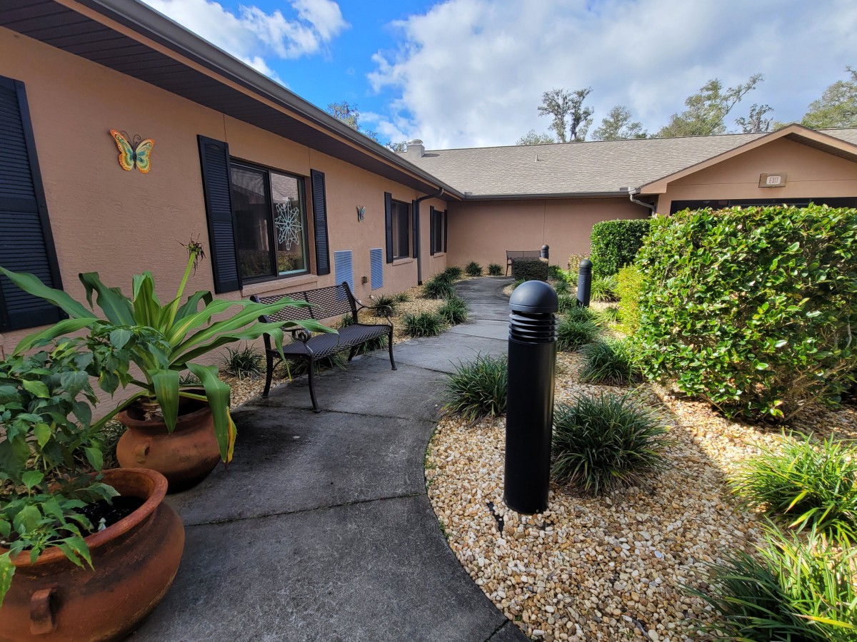 A peaceful courtyard with a pathway, surrounded by lush greenery and outdoor seating.