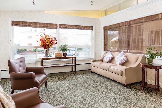 A cozy living room with a beige sofa and armchairs, complemented by a floral arrangement on a wooden table near large windows.
