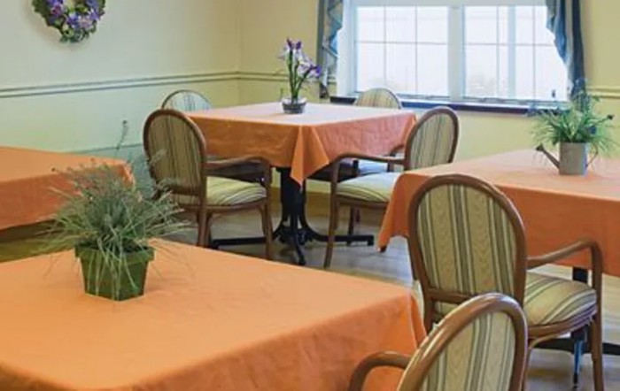 A cozy dining area with tables covered in orange tablecloths and wooden chairs.