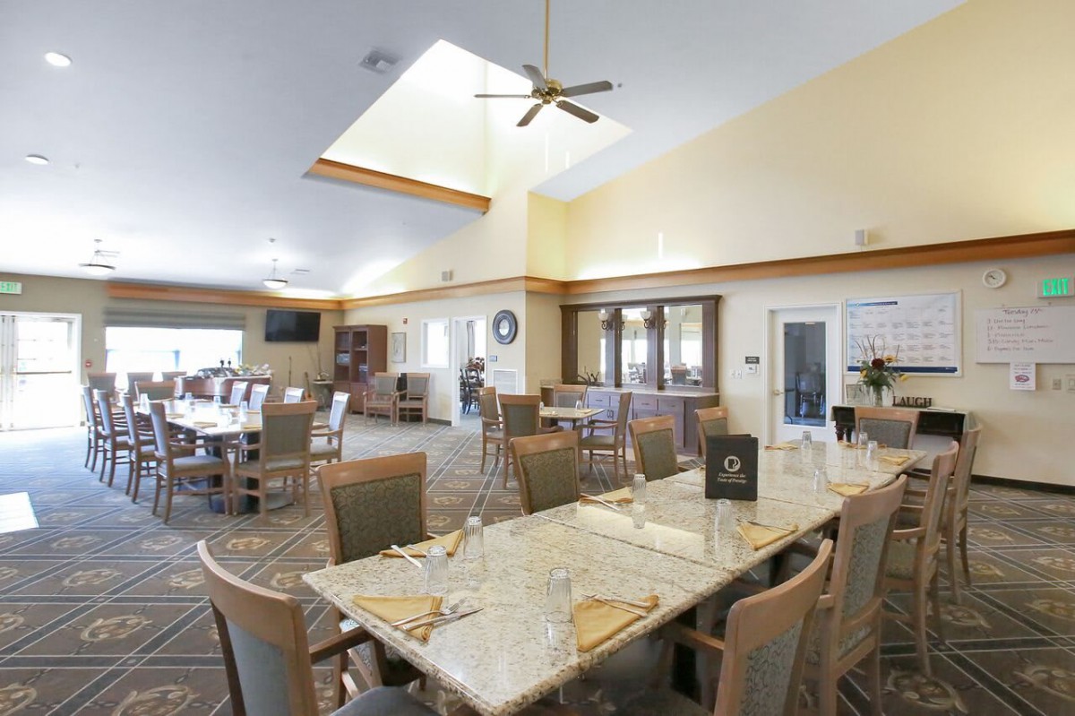 A spacious dining room with multiple tables and chairs, featuring a ceiling fan and bright lighting.