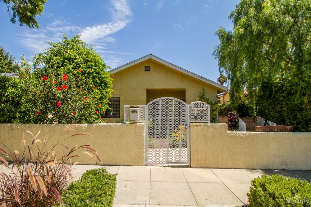 A charming house with a fenced front yard and lush greenery under a clear blue sky.