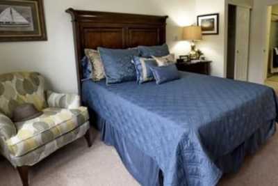 A cozy bedroom with a neatly made bed featuring blue bedding and decorative pillows, accompanied by a wooden nightstand and lamp.
