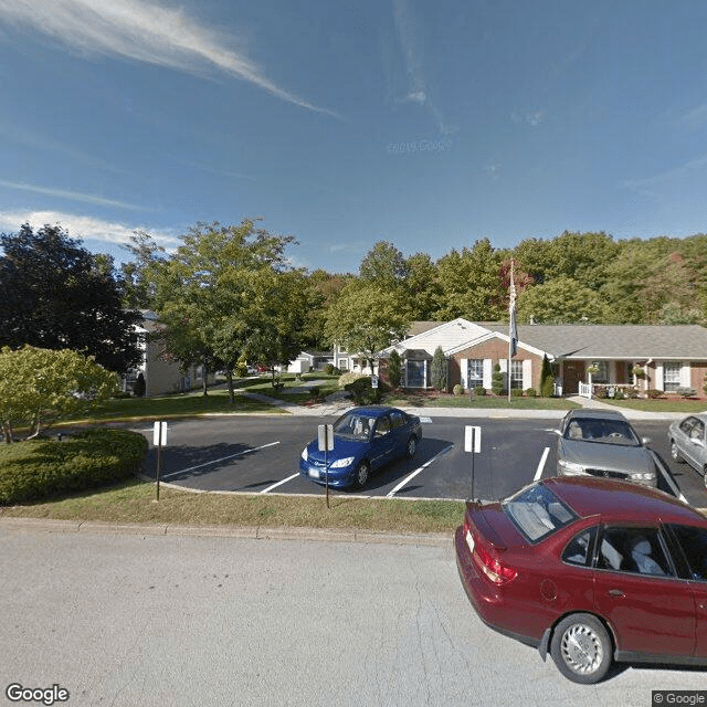 A small parking lot with a few cars in front of a building surrounded by trees under a partly cloudy sky.