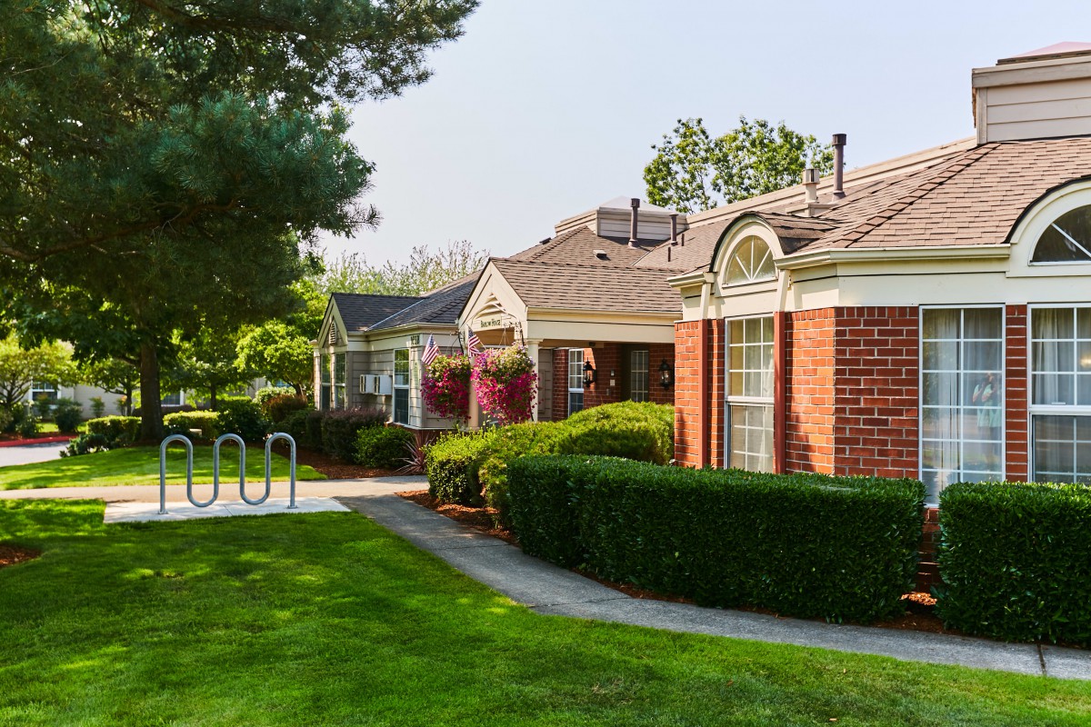 A charming residential area with brick buildings, manicured bushes, and a well-maintained pathway on a sunny day.