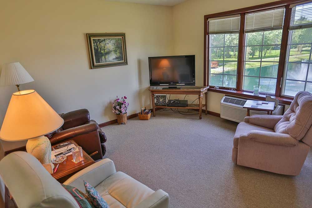 A cozy living room with a television, comfortable seating, and a large window offering natural light.