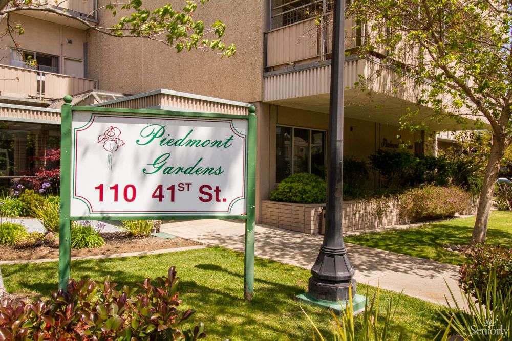 An apartment building with a sign reading 'Piedmont Gardens, 110 41st St.' surrounded by greenery.