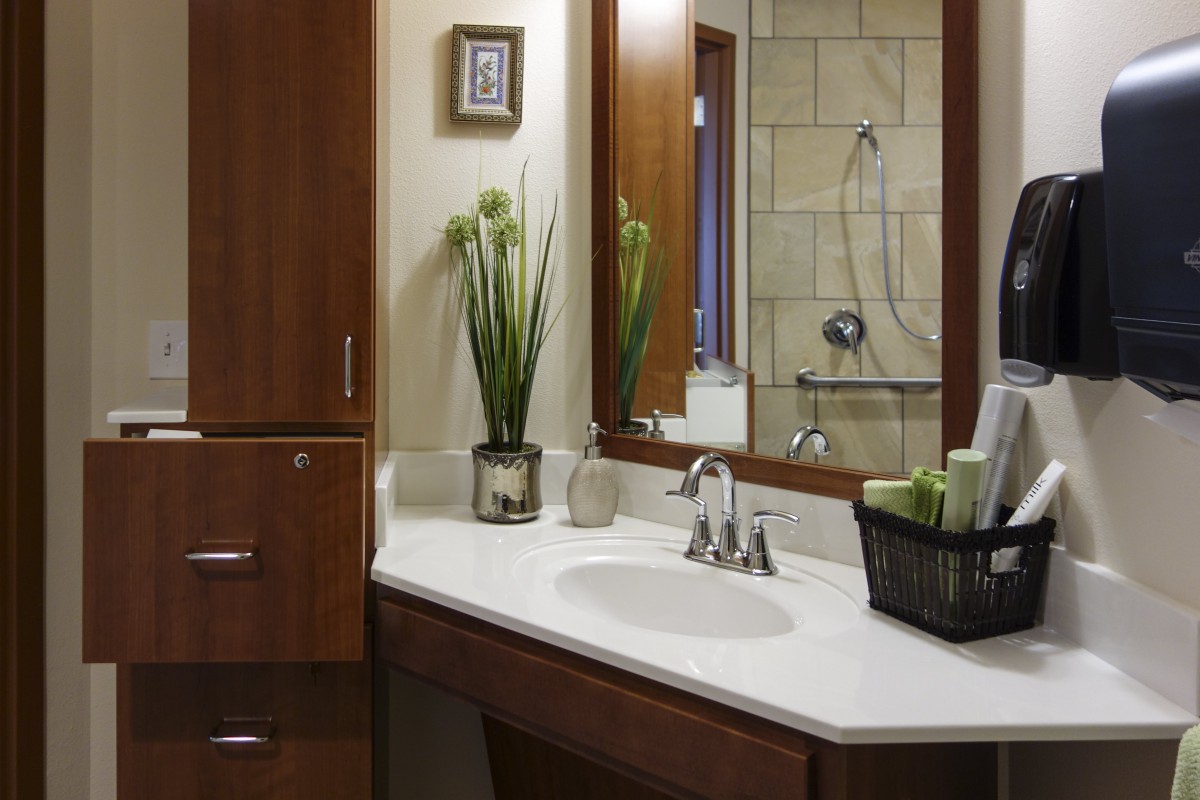 A modern bathroom with a wooden cabinet, mirror, and a neatly organized countertop featuring a vase with plants.