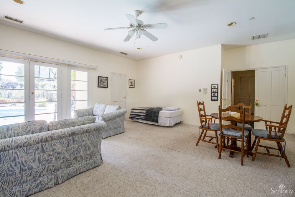 A bright living room with sofas, a dining table, and a ceiling fan.