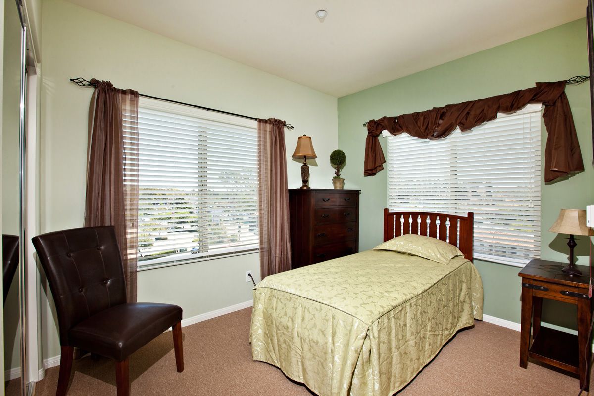 A cozy bedroom with a single bed covered in green bedding, surrounded by large windows with curtains.
