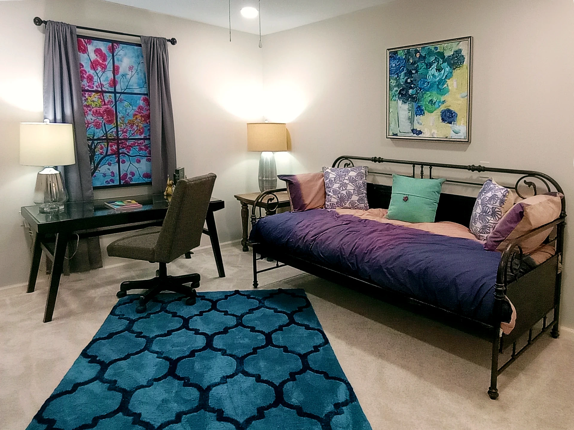 A cozy bedroom with a daybed, desk, and vibrant artwork.