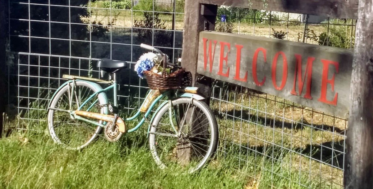 A vintage bicycle with a basket leans against a fence near a welcome sign.