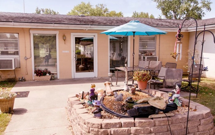 A cozy backyard patio with a blue umbrella and comfortable seating, surrounded by a small garden.